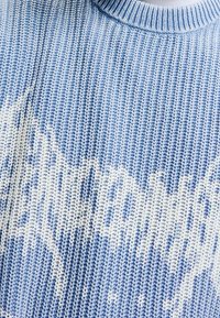 Stickad tröja i ljusblått med vitt abstrakt mönster. Har en ribbad rund halslinning och textil med struktur.