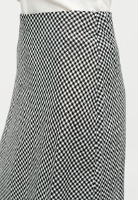 Jupe à motif vichy noir et blanc portée avec un haut blanc, raccourcie pour montrer la taille et la partie supérieure des hanches.