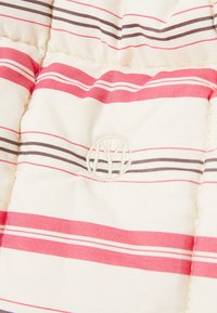 Gestreifter Stoff in Creme-, Rot- und Brauntönen; mit einem gestickten Logo in der Mitte; gesteppte Textur mit sichtbaren Nähten.