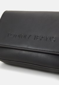Czarna skórzana kopertówka z wytłoczonym logo "TOMMY JEANS". Gładka faktura, prostokątny kształt, szyte krawędzie oraz zapięcie na klapkę.