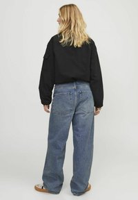 Svart oversized skjorte, blå vide jeans, lysebrune sneakers. Skjorten har lange ermer og en skulderlomme. Subtil denimtekstur.
