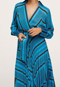 Vestido envolvente azul de manga larga con rayas marrones verticales y diagonales, un cuello y un lazo de tela en la cintura.
