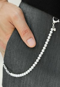 Silverkedja med vita pärlor fästa vid en ficka. Pärlorna är släta och sferiska, med en enhetlig färg längs kedjans längd.