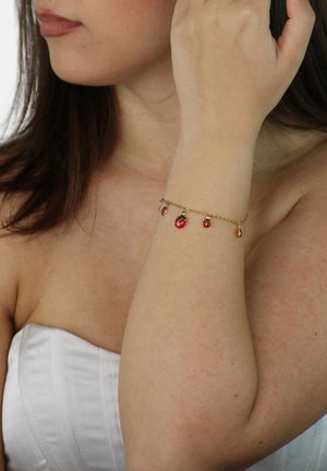 Bracelet en chaîne dorée ornée de cinq gemmes rouges, chacune suspendue avec une surface lisse, contrastant avec la peau. Design simple et délicat.