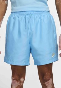 Ljusblå Nike träningsshorts med elastiskt midjeband och dragsko, bärs av en person med vitiligo på armar och ben.