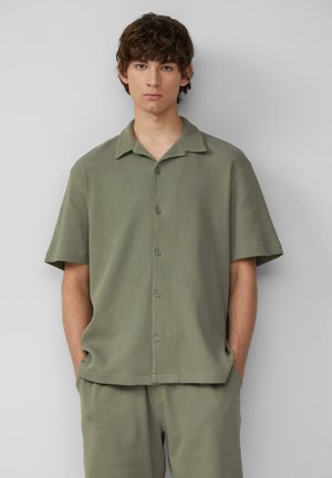 Olive green short-sleeve shirt with a textured, ribbed design, a button-down front, and a relaxed collar. Paired with matching pants.
