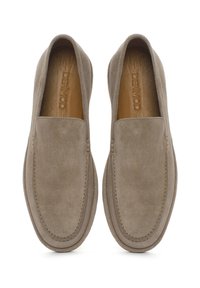 Zapatos slip-on de ante beige con punta redondeada, paneles laterales elásticos y costuras visibles a lo largo de los bordes, reposando sobre un fondo claro.