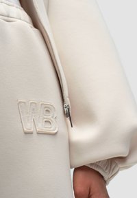 Cremfarbener Zip-Hoodie mit gesticktem "WB" in passendem Garn. Verfügt über gerippte Ärmelbündchen und eine weiche Stofftextur. Metallreißverschlussdetails.