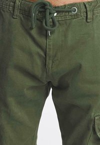 Zielone bawełniane spodnie cargo z elastyczną talią, sznurkiem do regulacji i bocznymi kieszeniami. Materiał jest gładki o naturalnym wykończeniu.