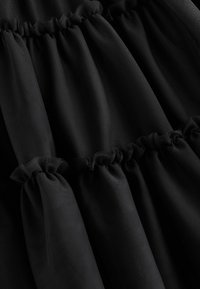 Tissu noir à plusieurs niveaux avec des accents de volants froncés, présentant une texture transparente et une finition lisse. Les couches créent une apparence vaporeuse.