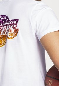 Vit bomull t-shirt med en grafisk logotyp i lila och orange med en baskettbolldesign. Kort ärm och avslappnad passform.