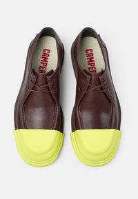 Scarpe in pelle marrone con punta arrotondata in gomma gialla, dotate di lacci e di una morbida fodera. Nome del marchio visibile all'interno della scarpa.