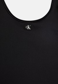 Fekete ujjatlan póló, kerek nyakkivágással és sima textúrával. A címkén fekete háttér előtt fehér "cK" logó látható, hangsúlyozva a minimalista megjelenést.