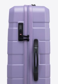 Valigia rigida di colore lavanda, con finitura testurizzata. Dotata di lucchetto a combinazione, zip robusta e manico nero su un lato.