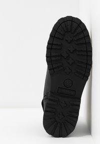 Suela de bota Timberland negra con un patrón de relieve profundo para tracción. El material parece goma con acentos texturizados. Logotipo visible en el área del talón.