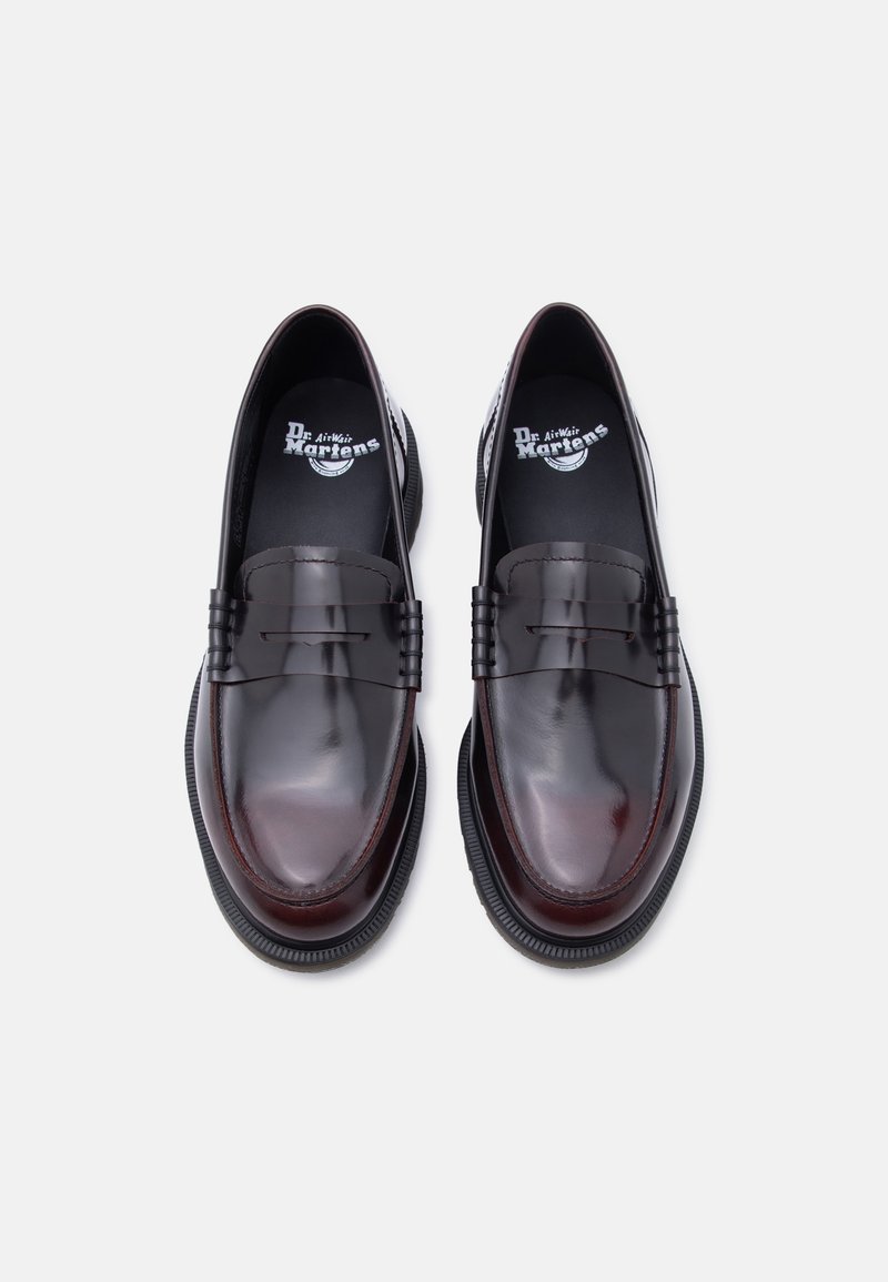 Paar glänzende dunkelburgunderrote Leder-Loafer von Dr. Martens mit dicken schwarzen Sohlen, von oben auf weißem Hintergrund gesehen.