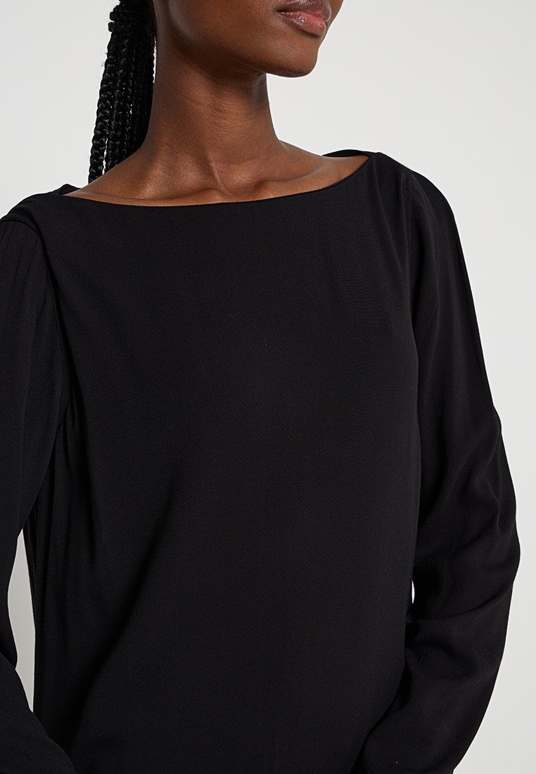 Maglietta nera a maniche lunghe con scollatura ampia a barca, caratterizzata da un tessuto testurizzato e spalle leggermente arricciate, che creano una silhouette rilassata.