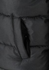 Sección de chaqueta tipo puffer negra con costuras acolchadas horizontales, un bolsillo lateral con cierre a presión y una textura de tela suave y brillante.