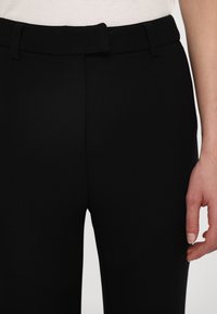 Black trousers featuring a smooth texture, a slim fit, and a standard waistband with a belt loop. The design is simple and classic.
