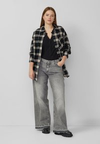 Zwart-wit geruit hemd met knopen over een zwart shirt, gecombineerd met vervaagde grijze wijde jeans en zwarte chunky schoenen.