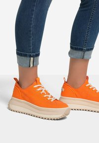 Oranssi kangaskengät, joissa on teksturoitu pinta, valkoiset nauhat ja paksu, uritettu pohja. Lahkeet käännettyinä sopivat hyvin kenkien kanssa.