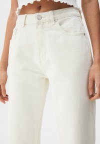 Pantaloni in denim bianco a vita alta con design a gamba dritta, dotati di chiusura frontale con bottone, cinque tasche e una texture sottile.