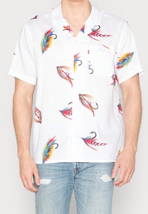 Camisa blanca de manga corta abotonada con estampados coloridos de moscas de pesca combinada con vaqueros azul claro rasgados.
