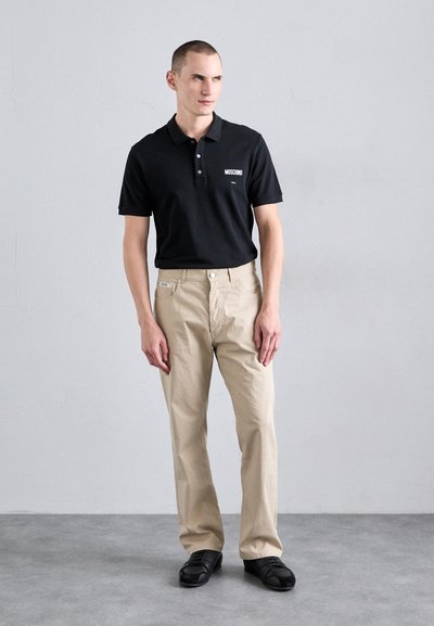 Black polo shirt with three buttons and "MOSCHINO" logo, paired with beige straight-leg pants and black leather shoes. Minimalistic design.