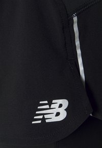 Svarta sportshorts med en reflekterande silverlogotyp och en sidopanel med en tunn silverrand. Tillverkade av ett mjukt, ventilerande tyg.