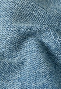 Denim tyg i ljusblått, med en synlig vävning och små texturvariationer, visas i en skrynklig, hängande position.