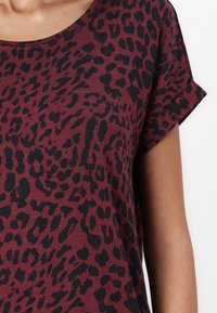 T-shirt bordeaux avec un imprimé léopard noir, à manches courtes, avec un col rond, en coton doux, avec des détails de couture subtils.