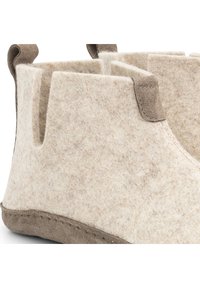 Vilt pantoffels in lichtbeige met een zachte textuur, voorzien van bruine suède accenten en zijopeningen voor gemakkelijk aan- en uittrekken. Geweven details langs de zool.