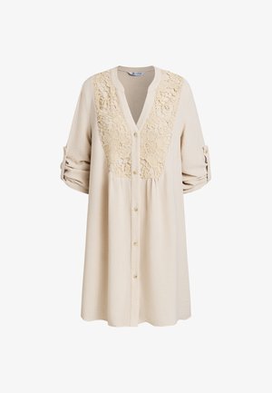 Robe beige à manches longues avec boutonnière, panneau en dentelle florale sur la poitrine et manches retroussées maintenues par des pattes boutonnées.