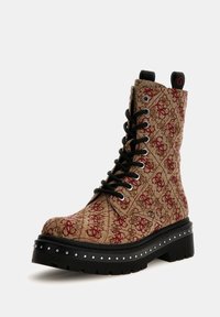 Bottine à lacets avec un tissu texturé de motifs marron et rouge, semelle en caoutchouc noir avec des clous décoratifs, et lacets noirs.