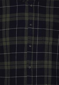 Camicia di flanella in blu navy e motivo a quadri verdi. Presenta una chiusura frontale con bottoni, maniche lunghe e una tasca sul petto con cuciture a contrasto.
