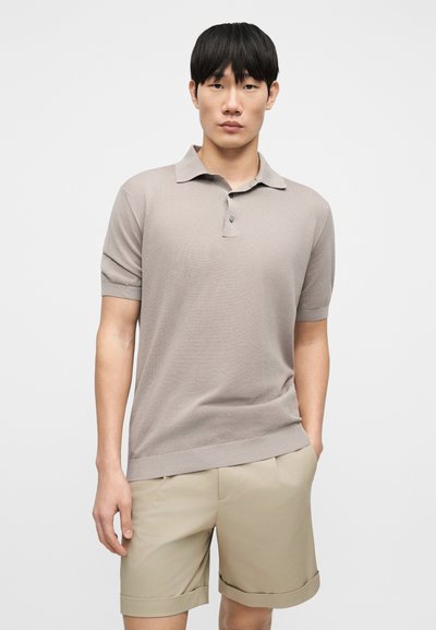 Μπεζ πλεκτό πόλο μπλουζάκι με κοντά μανίκια και τρία κουμπιά, σε συνδυασμό με ανοιχτό μπεζ, ραμμένο σορτς με διπλωμένο τελείωμα. Απλός σχεδιασμός.