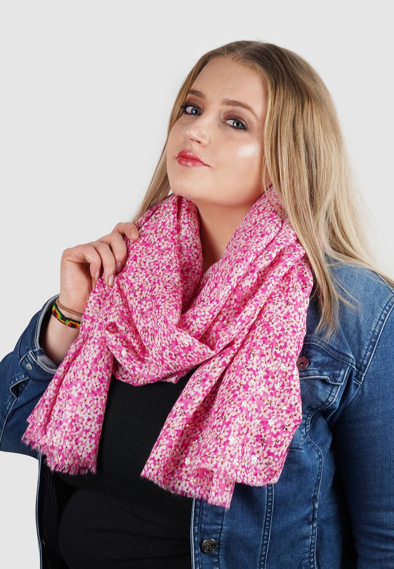 Roze sjaal met bloemmotief van lichtgewicht stof, met franjes aan de randen. Casual om de nek gedragen, ter aanvulling van een informele denim look.