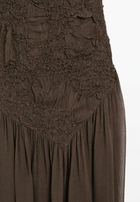 Brown fabric with gathered, ruched, and textured sections above a pleated, semi-sheer lower portion.