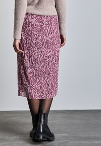 Gonna midi plissettata rosa con un audace motivo astratto, realizzata in tessuto leggero; indossata con stivali alla caviglia neri e collant trasparenti.