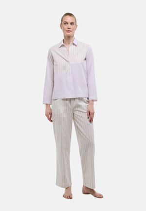 Femme debout, pieds nus, portant une chemise à manches longues boutonnée et un pantalon assorti à rayures dans des couleurs pastel claires.