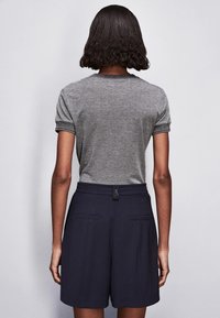 Camicia grigia a maniche corte con orli arrotolati, abbinata a pantaloni corti blu navy a vita alta con tasche anteriori e chiusura a bottone discreta.