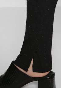 Zwarte geribde gebreide broek met zijslits, met een subtiele glans. Gecombineerd met een glanzende zwarte blockhak sandaal.