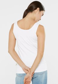 White cotton tank top with a scoop neckline and wide straps, featuring a fitted shape and a straight hem. Worn with light denim jeans.