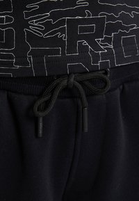 Zwarte katoenen joggers hebben een gestructureerde tailleband met een trekkoord. De stof heeft een gladde afwerking, met een contrasterend grafisch ontwerp op het shirt.