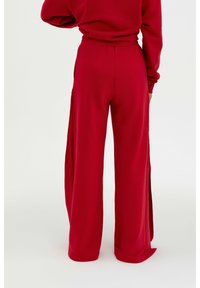 Rote, weit geschnittene Hosen mit einem bequemen, elastischen Bund. Der Stoff scheint weich zu sein und verfügt über Seitenschlitze für zusätzliche Luftzirkulation und Stil.