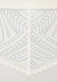 Weißes Spitzenkleidungsstück mit komplizierten Mustern und gewellten Kanten, oben aus glattem Stoff und unten mit detaillierter Spitzenstruktur.