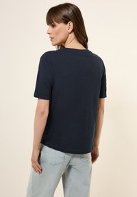 T-shirt bleu marine à manches courtes avec un col rond et une coupe décontractée, associé à un jean en denim bleu clair et à une texture lisse.