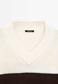 Maglione lavorato a maglia con scollo a V, in cima di un colore crema chiaro, con una striscia orizzontale di crema, e una parte inferiore marrone scuro. Etichetta visibile.