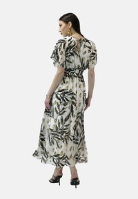 Robe maxi en tissu léger, ornée d'un motif floral avec des feuilles vertes et des accents jaunes. Elle a des manches courtes et une taille cintrée.