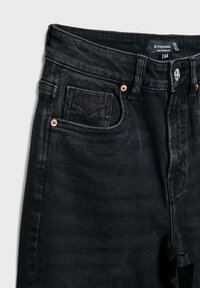 Crne traperice s visokim strukom, koje imaju dizajn s pet džepova, bakrene kopče i teksturiranu tkaninu za veću izdržljivost.